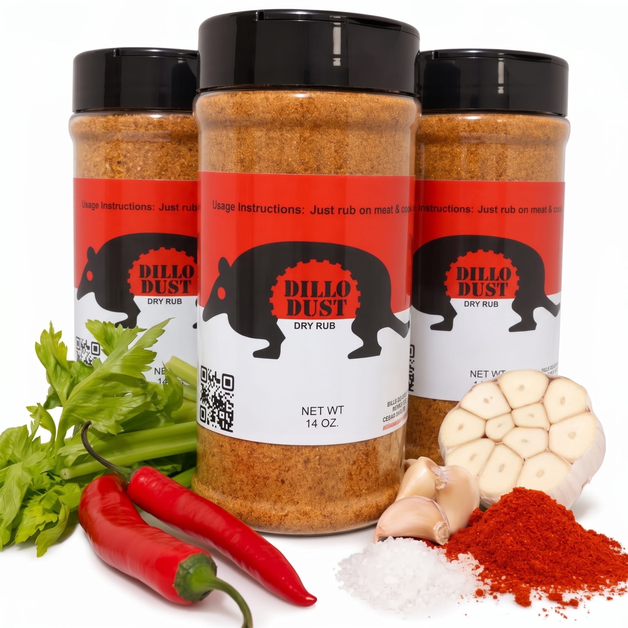 Three bottles of Dillo Dust Dry Rub BBQ seasoning arranged on a white surface with fresh celery, red chili peppers, garlic cloves, sea salt, and paprika.